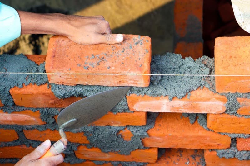 Bricklayer laying a brick on fresh mortar with a trowel