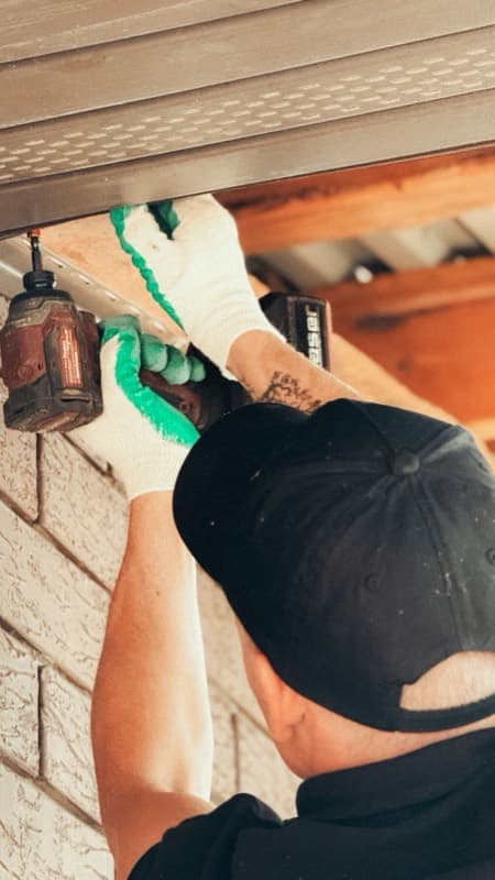 Handyman with a cordless drill fitting an outdoor light under the eaves