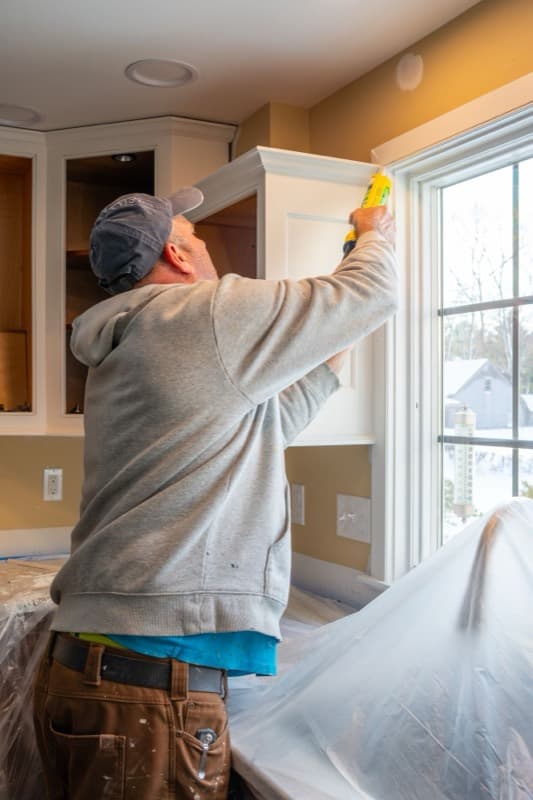 Fitter sealing a new kitchen cabinet by a window