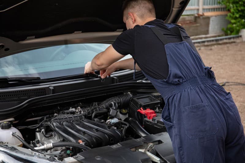 Mechanic in overalls working on a car engine outdoors