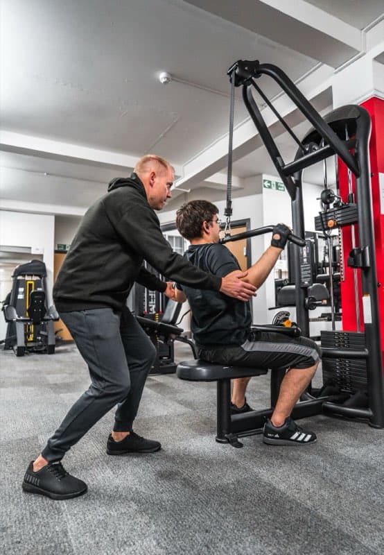 Personal trainer guiding a client through a pull-down on a gym machine