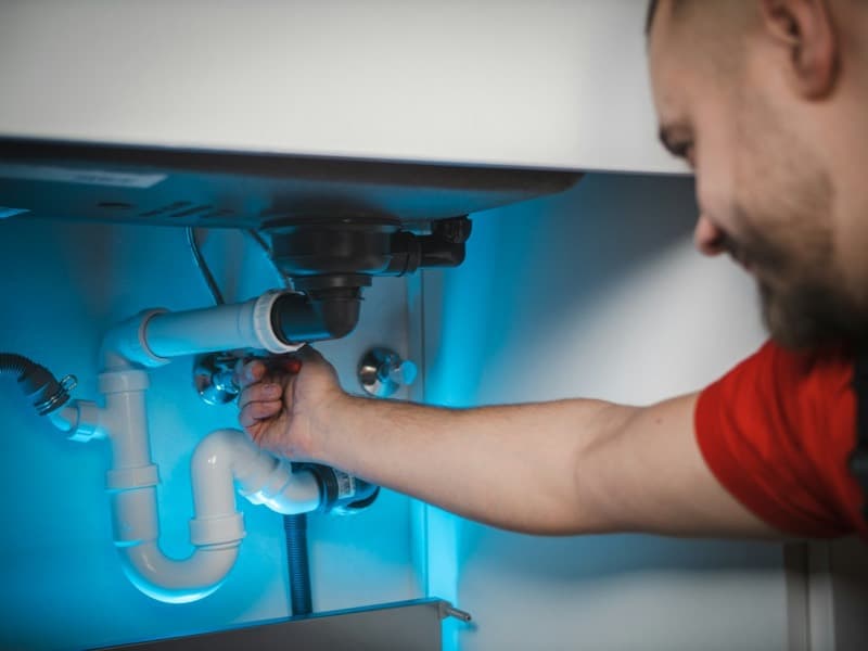 Plumber reaching under a sink to fix the waste pipe
